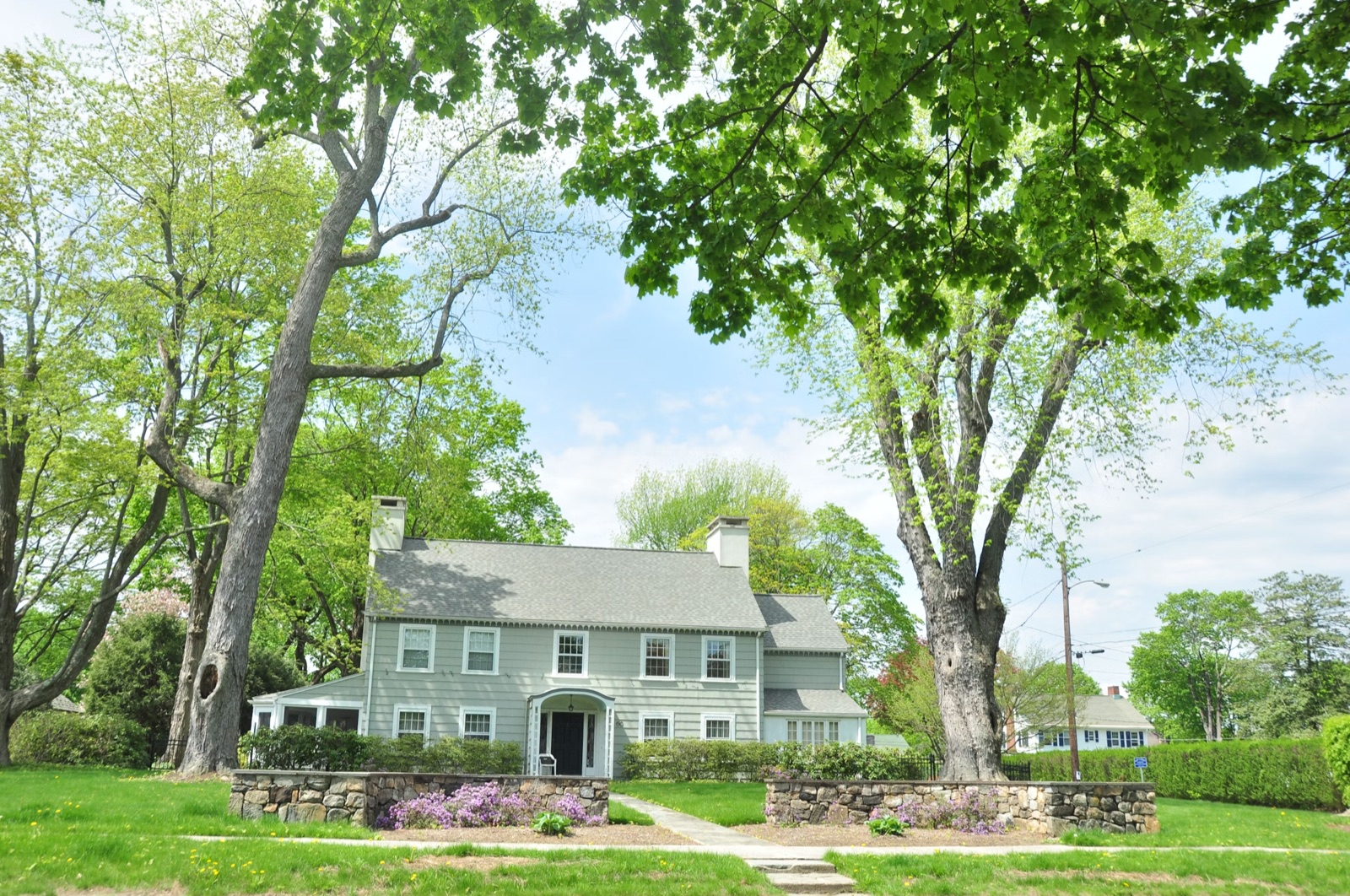 Sage-green colonial with a manicured lawn and fieldstone walls